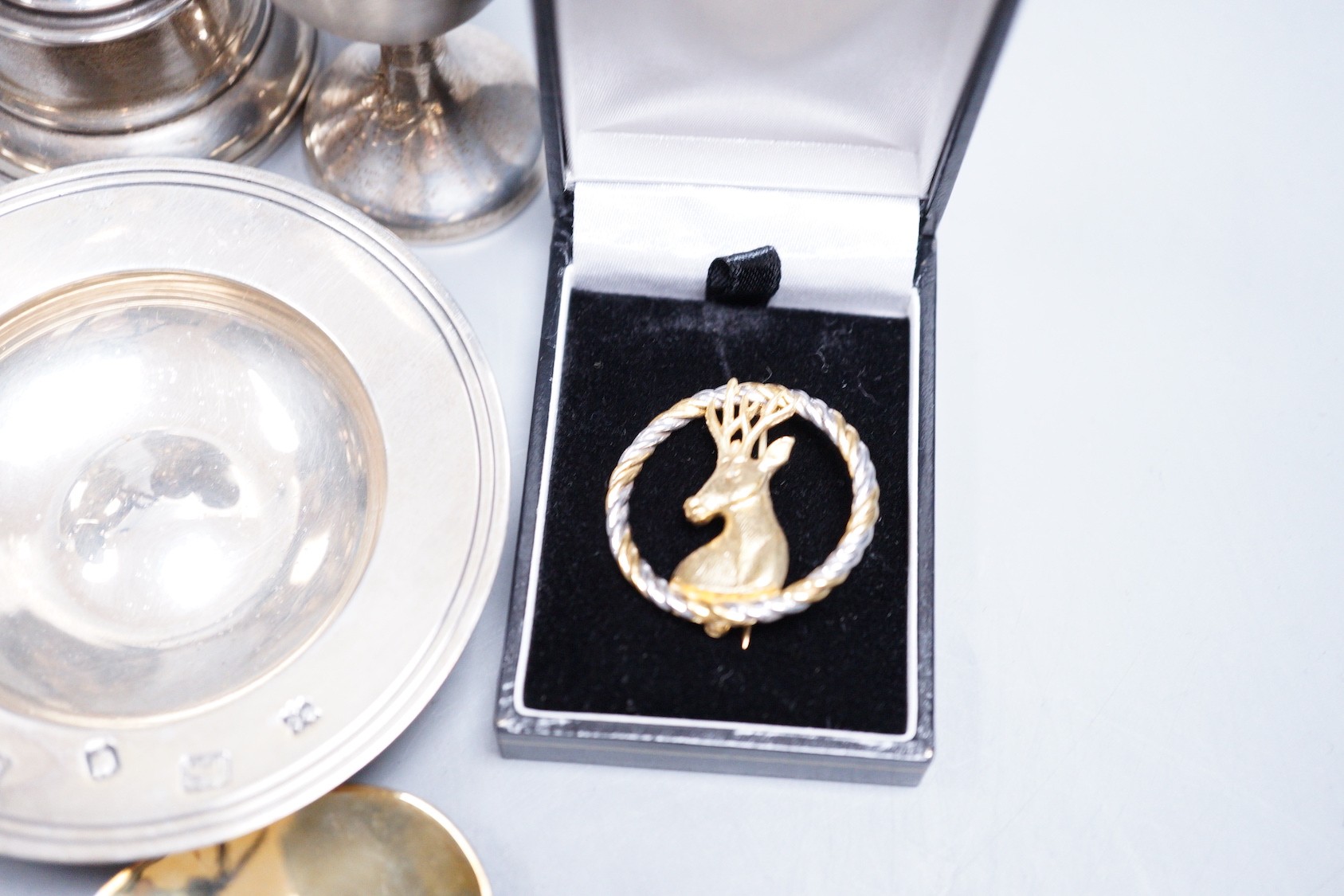 A small collection of assorted small silver, including a capstan inkwell, pair of dwarf candlesticks, two small trophy cups, egg cup, flatware, napkin ring, glass caster, a modern parcel gilt silver stag brooch and three